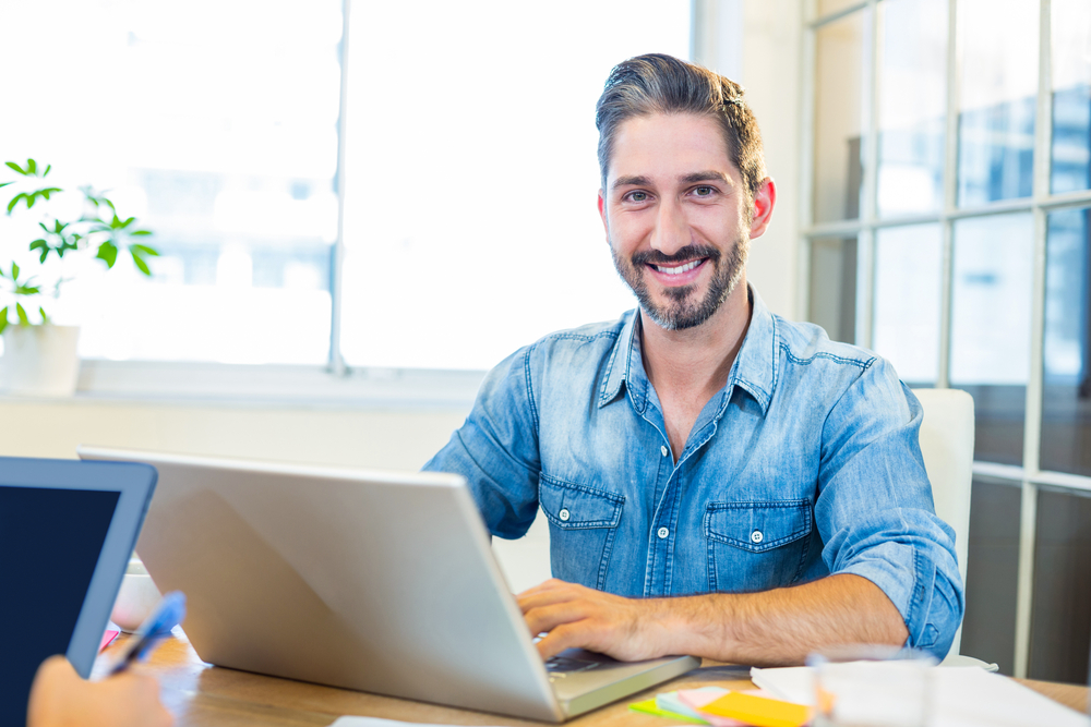 Man smiling and using laptop to choose scheduling software